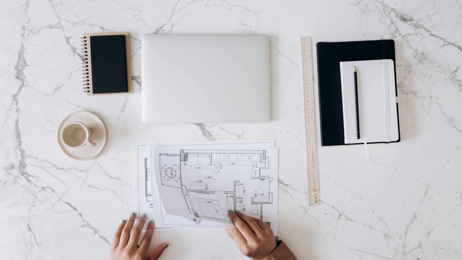 Overhead view of an architect's desk with floor plans, a laptop, ruler, and notebook