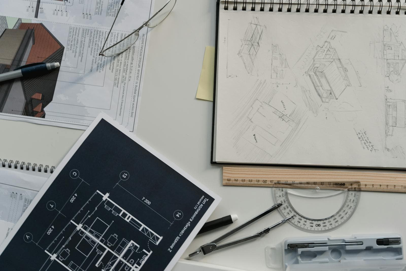 Overhead close-up of architectural floor plans with a sketchbook, ruler, and protractor