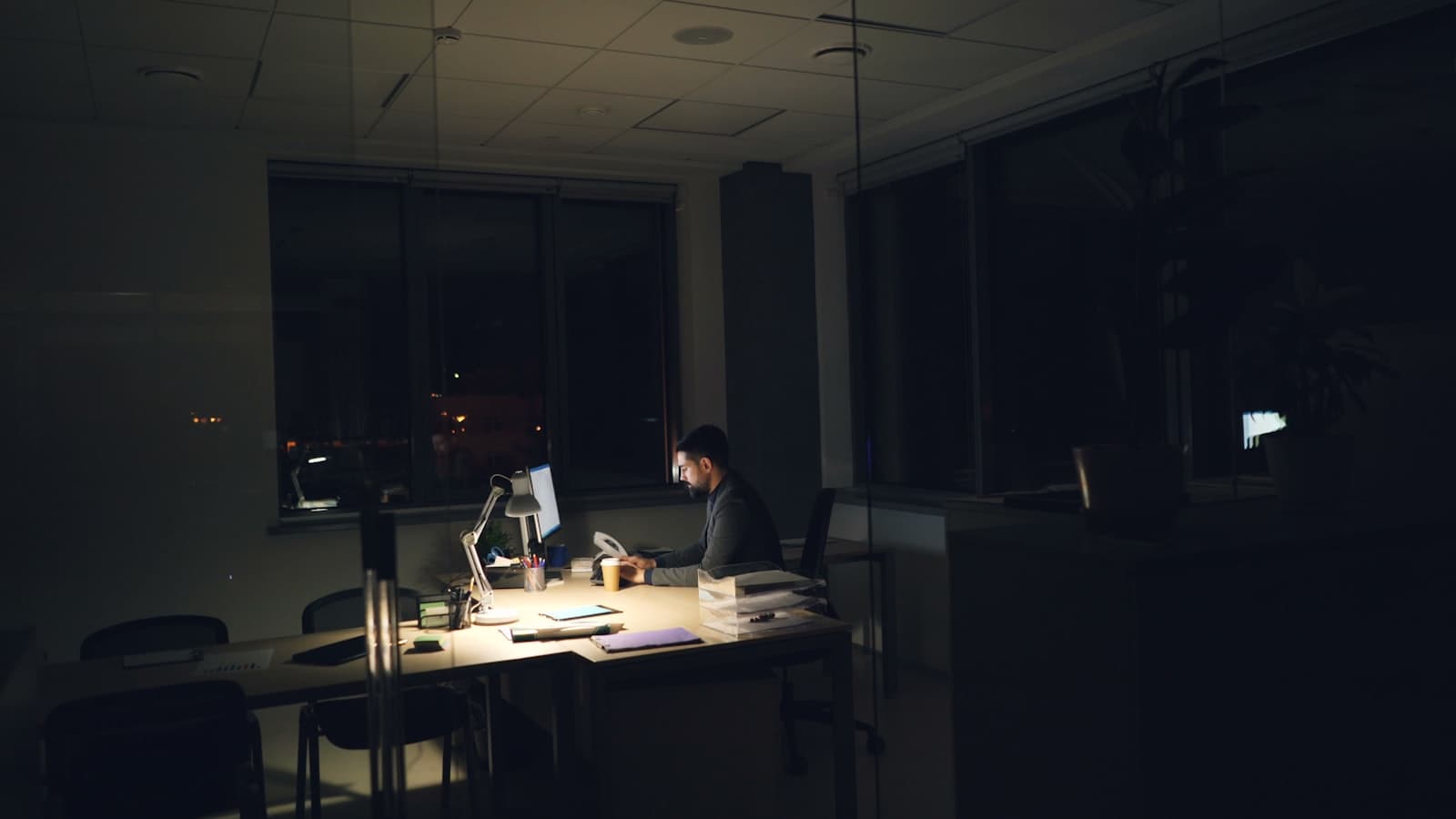 A person working alone at a desk in a dimly lit office at night