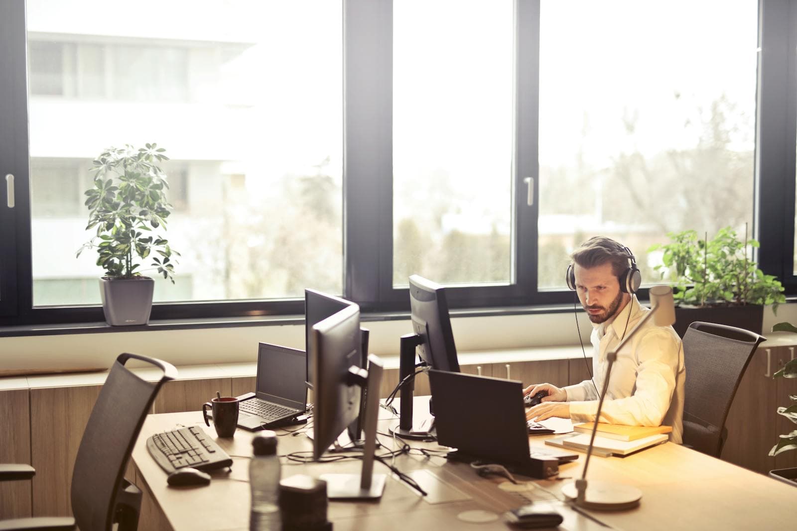 A sales rep with a headset focused at a multi-monitor workstation in natural office light